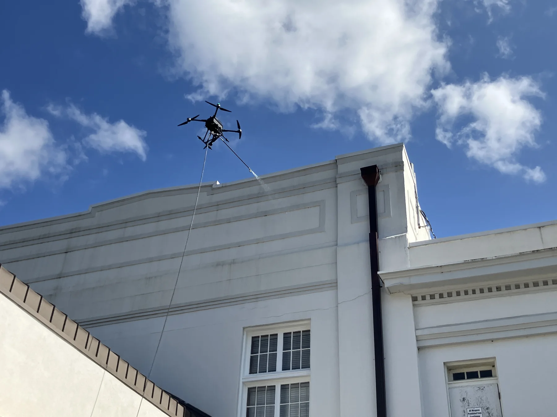 Commercial washing drone applying a rinse to a high building facade